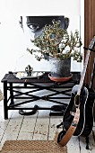 Gitarre auf Gitarrenständer, vor Blumenbank aus dunklem Bambus mit Zimmerpflanze