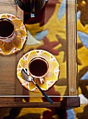 Espressotassen und Untertassen mit Blütenmuster auf Glastisch
