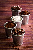 Verschiedene Kaffeearten: Kaffeebohnen, Pulver, Kapseln, Löskaffee, Sachets in Metallbechern