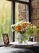 Posy of ranunculus and viburnum in glass vase on windowsill