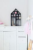 House-shaped, dark metal display case on top of white, vintage cabinet