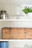 Vintage wooden crate stencilled in Swedish, tins and cake stand with glass cover on shelves
