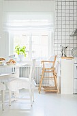 Dining area with ruched seat cushions, and high chair below window in white, Scandinavian kitchen
