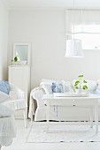 White seating area with country-house sofa, wicker chairs and shabby-chic lamp above coffee table