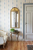 Gerahmter Spiegel über Konsolentisch mit geschwungenen Beinen, an tapezierter Wand mit weiss-blauem Muster