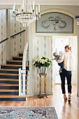 Foyer with white and blue wallpaper, curved staircase, bouquet and woman carrying baby