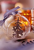 Transparent Christmas tree bauble with deer and Christmas tree figures inside decorating table (close-up)