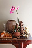 Ethnic, wooden figurines next to glass carafes and beakers on tray and pink orchid on console table