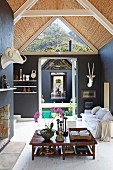 Low wooden table in open-plan interior with pale sofa, black-painted walls and exposed roof structure with bamboo interior cladding