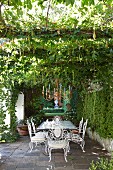 Ornate, white metal chairs around table on terrace and candle chandelier hanging from pergola