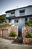 View from street of contemporary, multi-storey house with grey-painted façade and stone garden wall