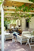 Sitzmöbel auf Terrasse unter berankter Pergola, vor ländlichem Holzhaus