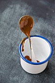 Caramel cream on a spoon in an enamel mug
