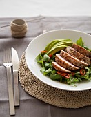 Grilled tuna on a bed of lettuce with avocado and peppers