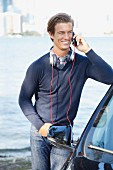 Junger Mann in Pullover mit Kopfhörer und Telefon neben einem Auto