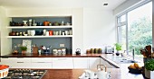 Shelves of crockery in grey-painted niche and U-shaped kitchen counter with wooden worksurface