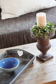 White candle in candlestick with wreath of flowers next to blue ceramic bowl on tray
