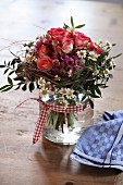 Posy of roses and daisies in glass jar decorated with gingham ribbon