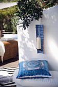 Blue and white patterned cushion on bench and candle in ceramic candle holder hung on wall of Mediterranean terrace