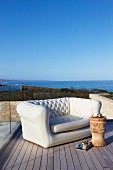 Elegant sofa and stool used as side table on wooden deck with sea view