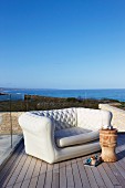 Elegantes Polstersofa und Beistellhocker auf Holzterrasse mit Meerblick