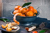 An arrangement of clementines in a metal bowl on a rustic wooden table