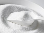 A bowl of white sugar with a scoop