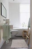 Modernes Bad mit Desigerwanne vor Fenster; Hocker und Handtuchleiter aus Naturholz