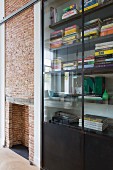 Fitted shelving with welded steel and glass doors next to fireplace in brick wall