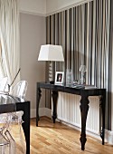 Postmodern, black console table and table lamp with white lampshade against wall with striped wallpaper in various shades of grey
