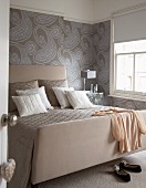 Double bed with upholstered headboard against wall with paisley wallpaper in bedroom in various shade of grey