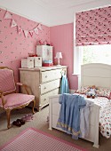 Girl's bedroom with pink patterned wallpaper and fabrics combined with white, country-house furnishings and antique armchair