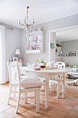 White kitchen chairs around dining table in pale grey dining room with tiled floor and chandelier