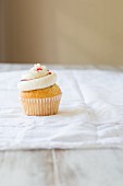 A vanilla cupcake topped with a vanilla cream, berries and sprinkles