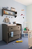 Changing table painted grey brown below matching shelves on wall painted pale blue and white rocking chair in corner to one side