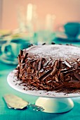 Chocolate cake with grated chocolate and icing sugar on a cake stand