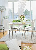 Spring atmosphere in bright dining room - modern chairs around white dining table in front of balcony doors, pile of cushions on floor in foreground