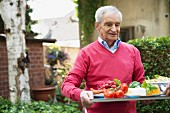 Älterer Mann trägt Tablett mit Speisen in den Garten