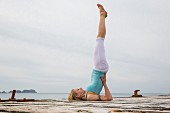 Frau macht Gymnastikübung auf Bootssteg am Meer