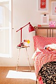 Vintage Hocker und rot lackierte Retroleuchte, daneben Bett mit gepunkteter Bettwäsche