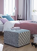 A patchwork pouffe as a bedside table or a seat next to a bed with a lilac bedspread