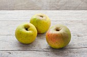 Drei Bio-Äpfel der Sorte Benheimer auf Holzuntergrund