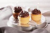 Three birthday cupcakes with lighted candles