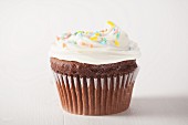 A chocolate cupcake with white frosting and sugar sprinkles