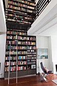 Two-storey bookcase and white bicycle on integrated gallery above Eames chair