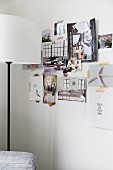 Stehleuchte mit weißem Lampenschirm vor Collage mit Fotos aus Zeitschriften an weißer Wand