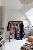 Black clothes rack next to vintage cabinet in corner of bedroom with sloping ceiling
