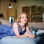 Blonde girl lying on bed with bottle of soda, looking up