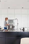 Woman in designer kitchen between dark base units and white fitted cupboards