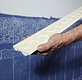 Anbringen einer Stuckleiste als Abschluss, über Lincrusta (Strukturtapete aus linoleumähnlichem Material) an Wand